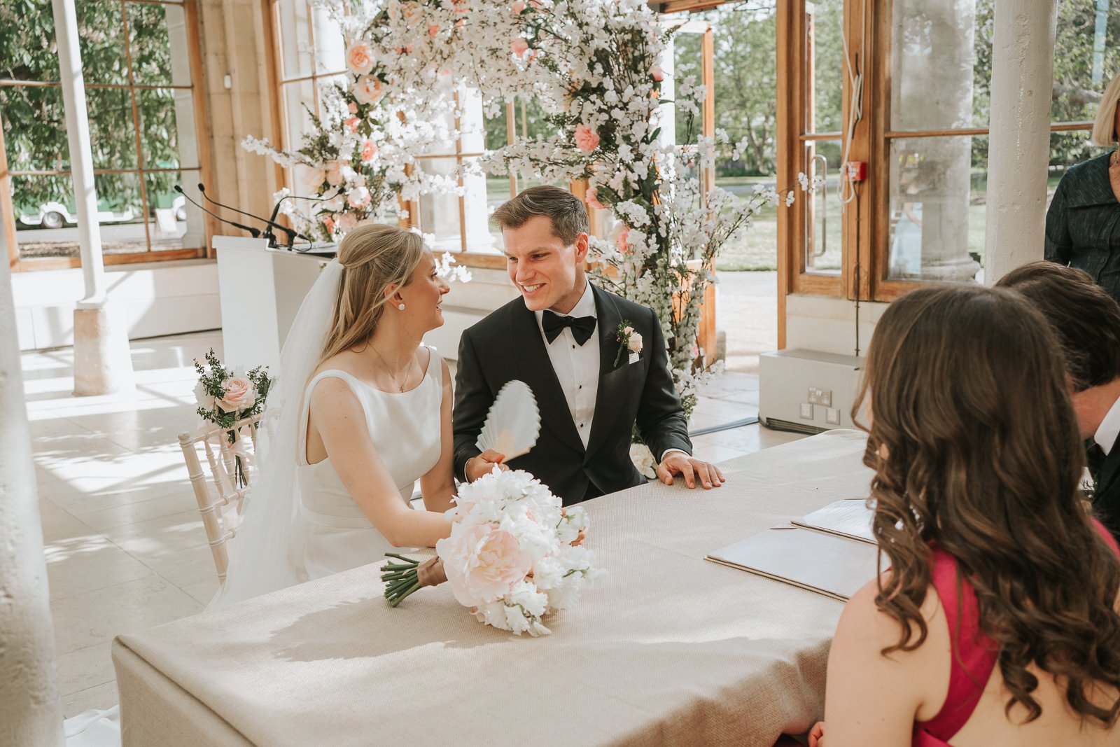  Bride and groom seated at the signing table after their ceremony in the sunlit Nash Conservatory at Kew Gardens. 