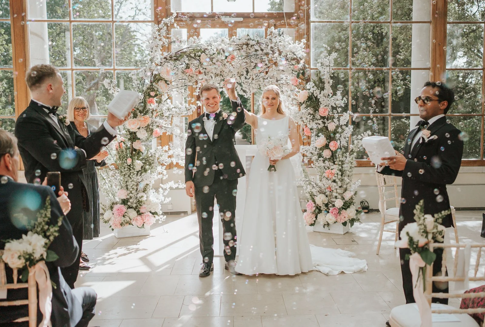  Bubble exit inside the Nash Conservatory at Kew Gardens as the newly married couple celebrate beneath a blossom-filled floral installation. 