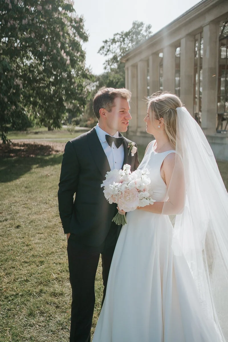  Elegant wedding portrait of the bride and groom beside the Nash Conservatory at Kew Gardens, surrounded by summer gardens and natural light. 