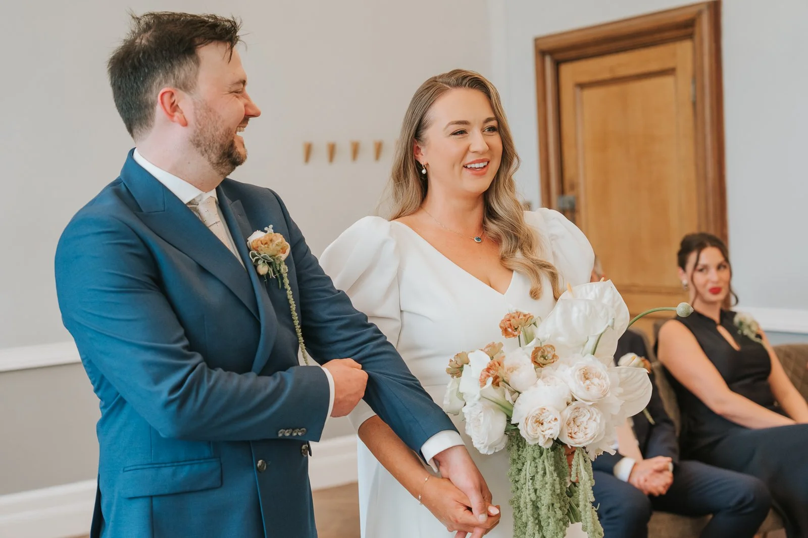  Bride and groom smiling during their wedding ceremony in Room 99 at Islington Town Hall surrounded by close family and friends. 
