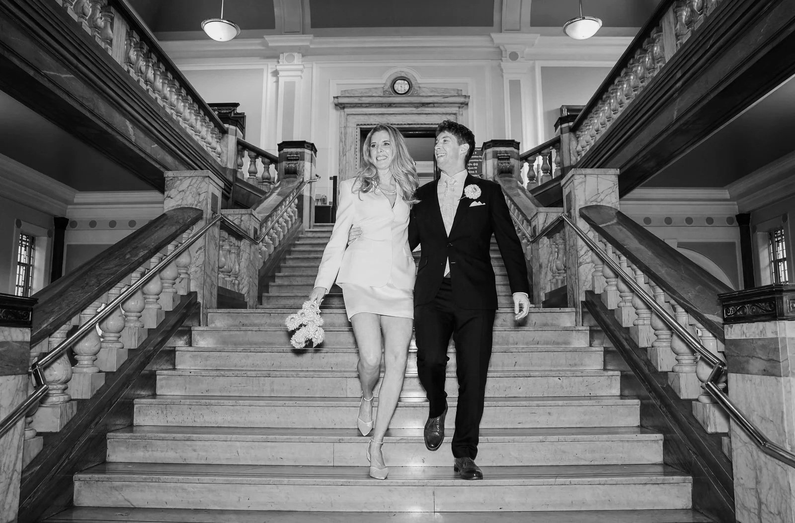  Bride and groom walking down the marble staircase inside Islington Town Hall after their wedding 