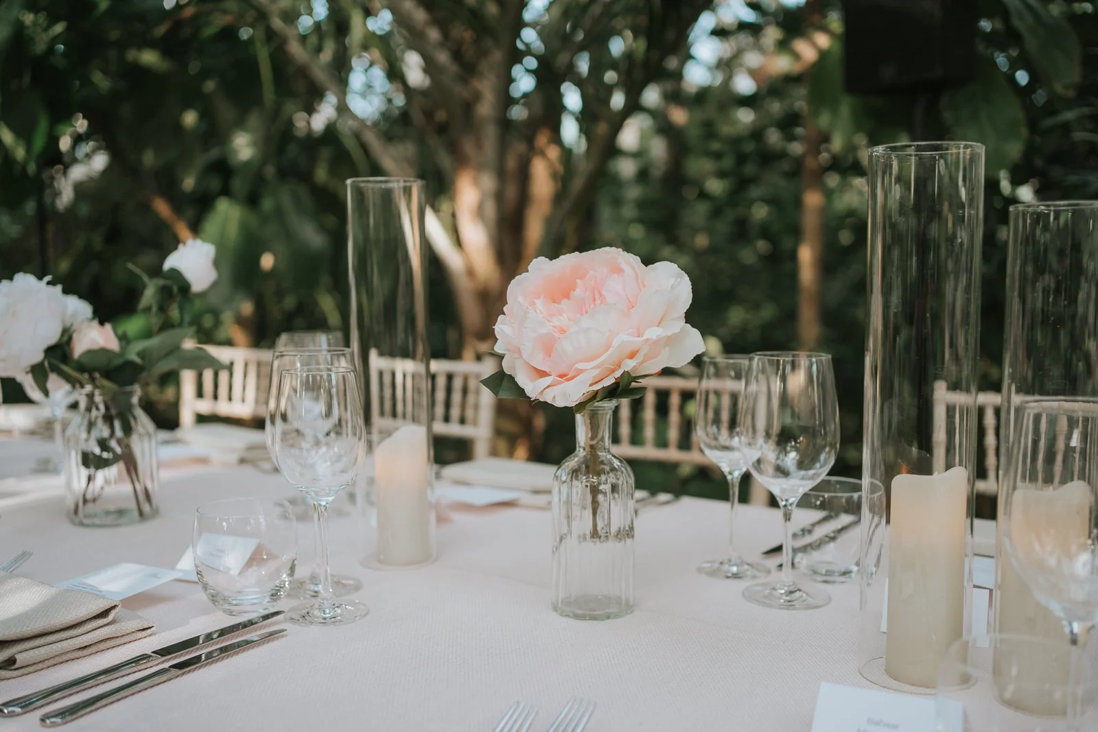  Close-up of wedding reception table styling in the Temperate House at Kew Gardens, featuring delicate pink peonies, candlelight and elegant glassware. 