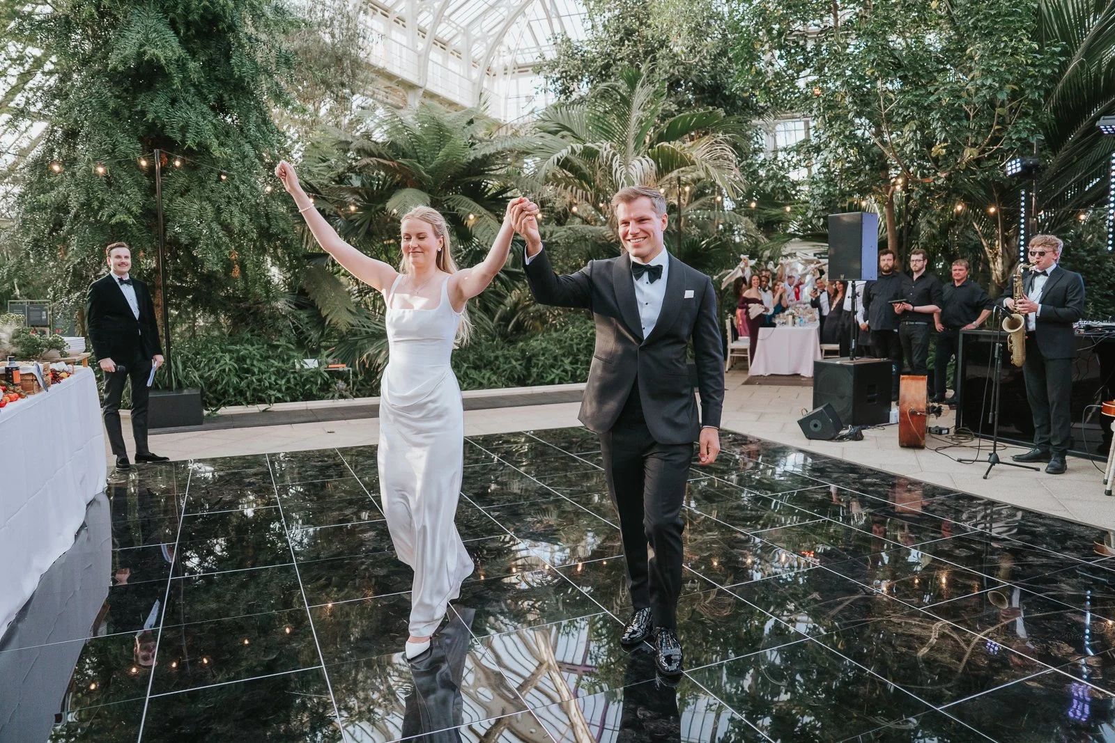  Newly married couple celebrating on the dance floor during their Temperate House wedding reception at Kew Gardens, surrounded by family, friends and live entertainment. 