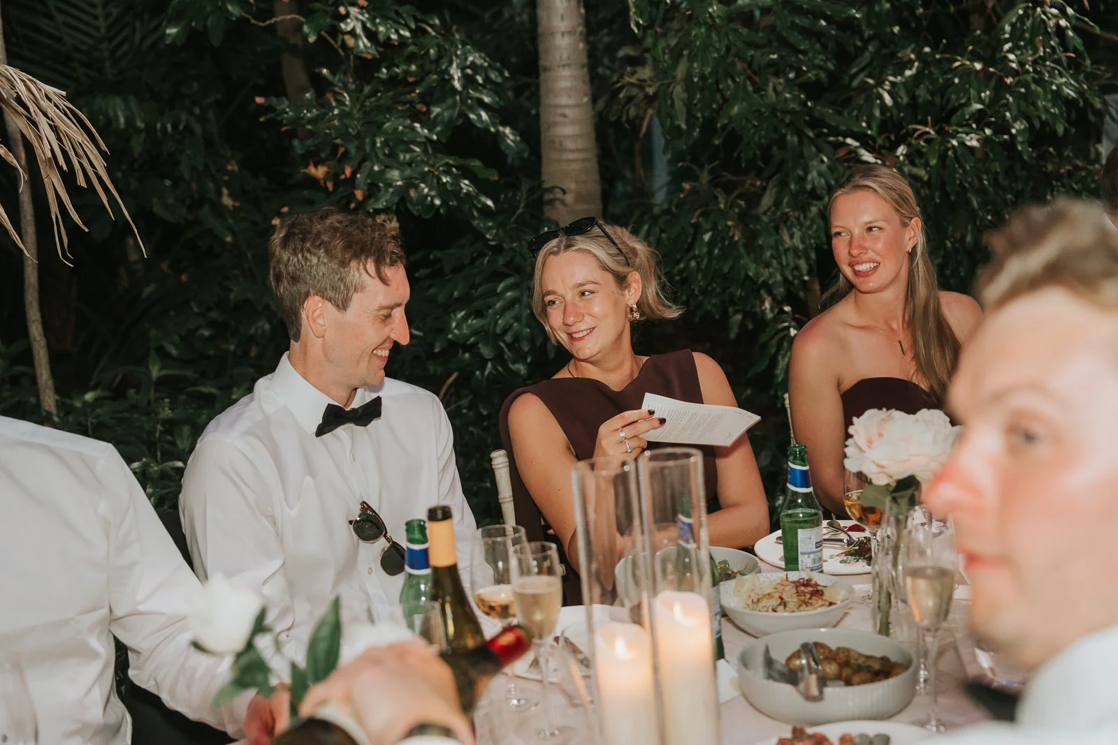  Guests laughing and chatting during wedding speeches in the Temperate House at Kew Gardens, seated among lush greenery and beautifully styled reception tables. 