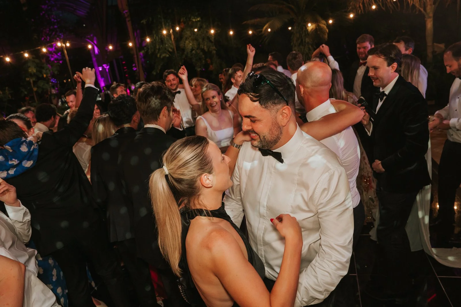  Wedding guests dancing and celebrating late into the evening in the Temperate House at Kew Gardens, surrounded by lush greenery and atmospheric lighting. 