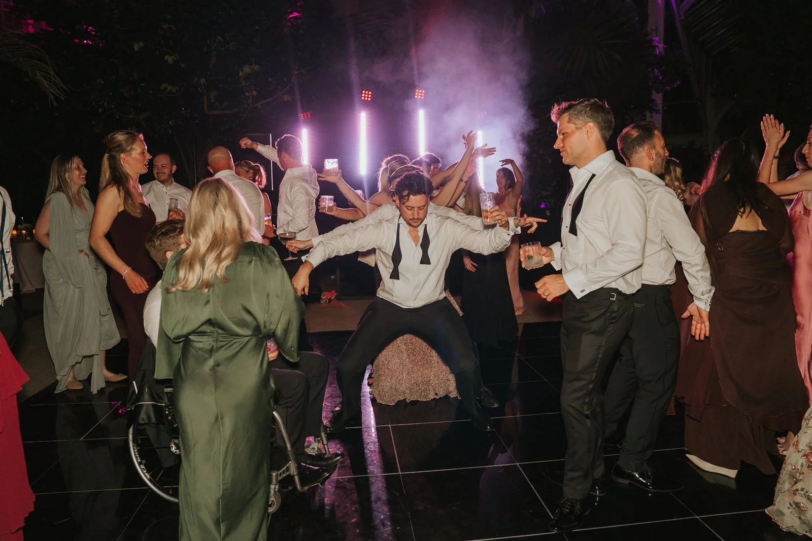  Guests dancing and celebrating beneath dramatic lighting in the Temperate House at Kew Gardens, creating a lively late-night wedding party atmosphere. 