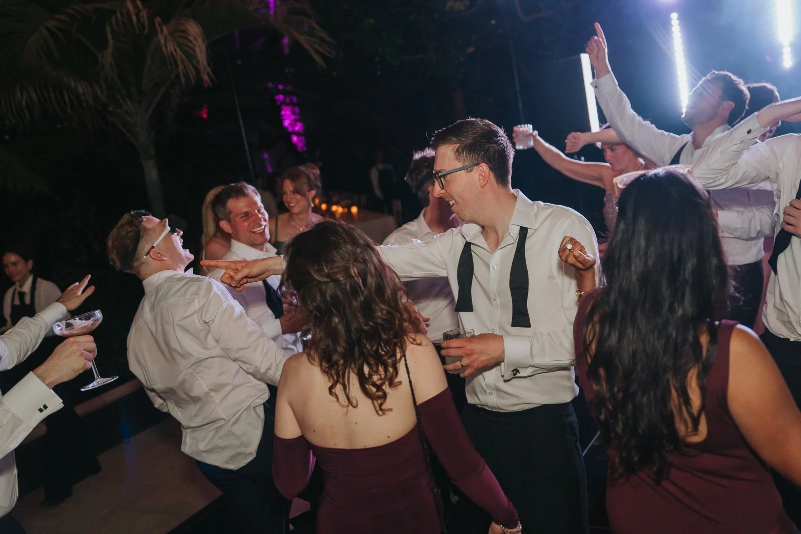  Guests dancing and celebrating beneath dramatic lighting in the Temperate House at Kew Gardens, creating a lively late-night wedding party atmosphere. 
