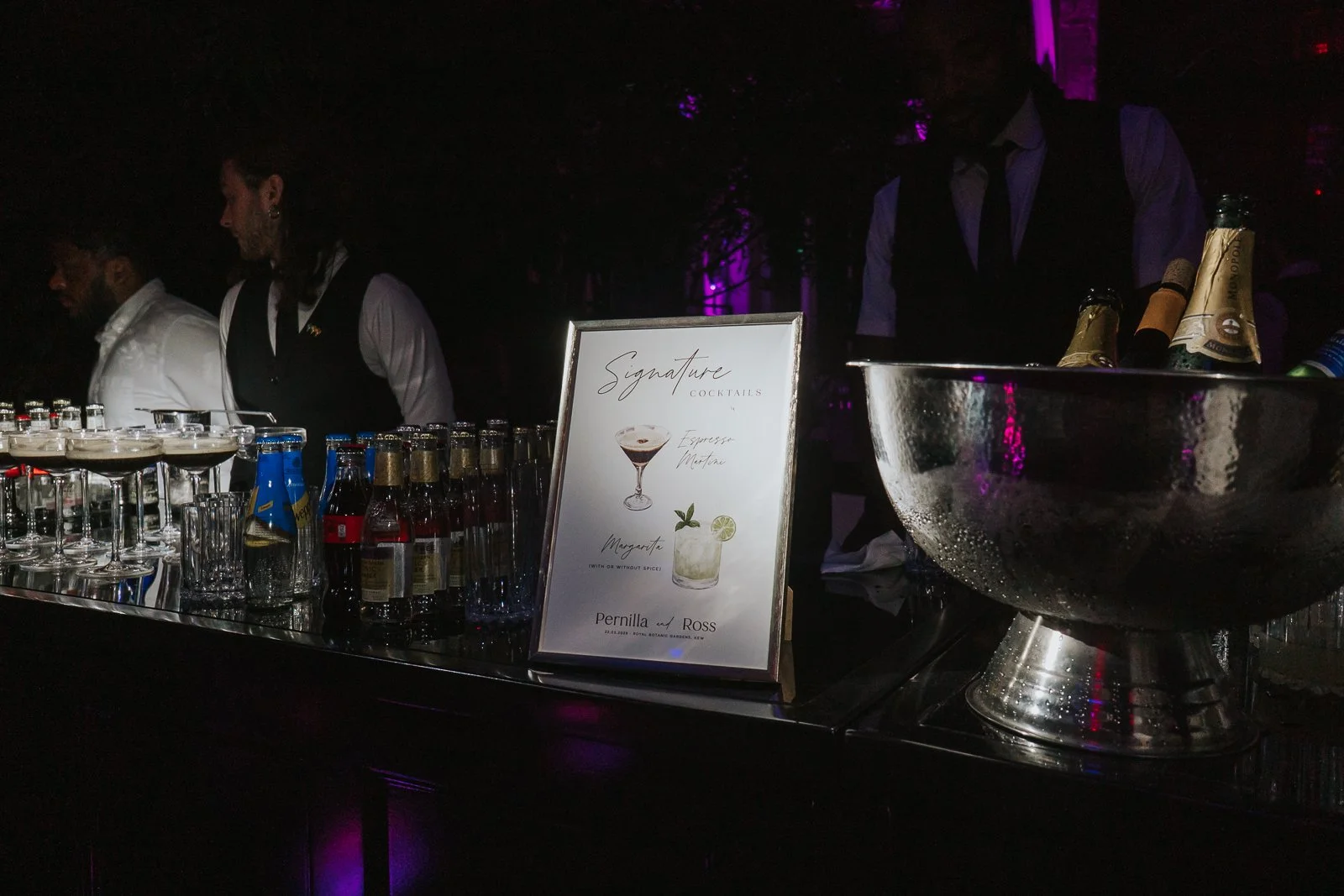  Signature cocktail bar setup at a wedding reception in the Temperate House at Kew Gardens, featuring personalised drinks, champagne and stylish evening décor. 