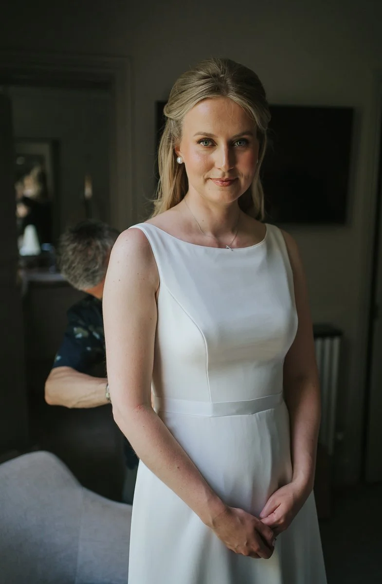  Elegant bridal portrait of a bride in a minimalist white wedding dress, photographed in soft natural light during preparations at The Petersham Hotel, Richmond. 