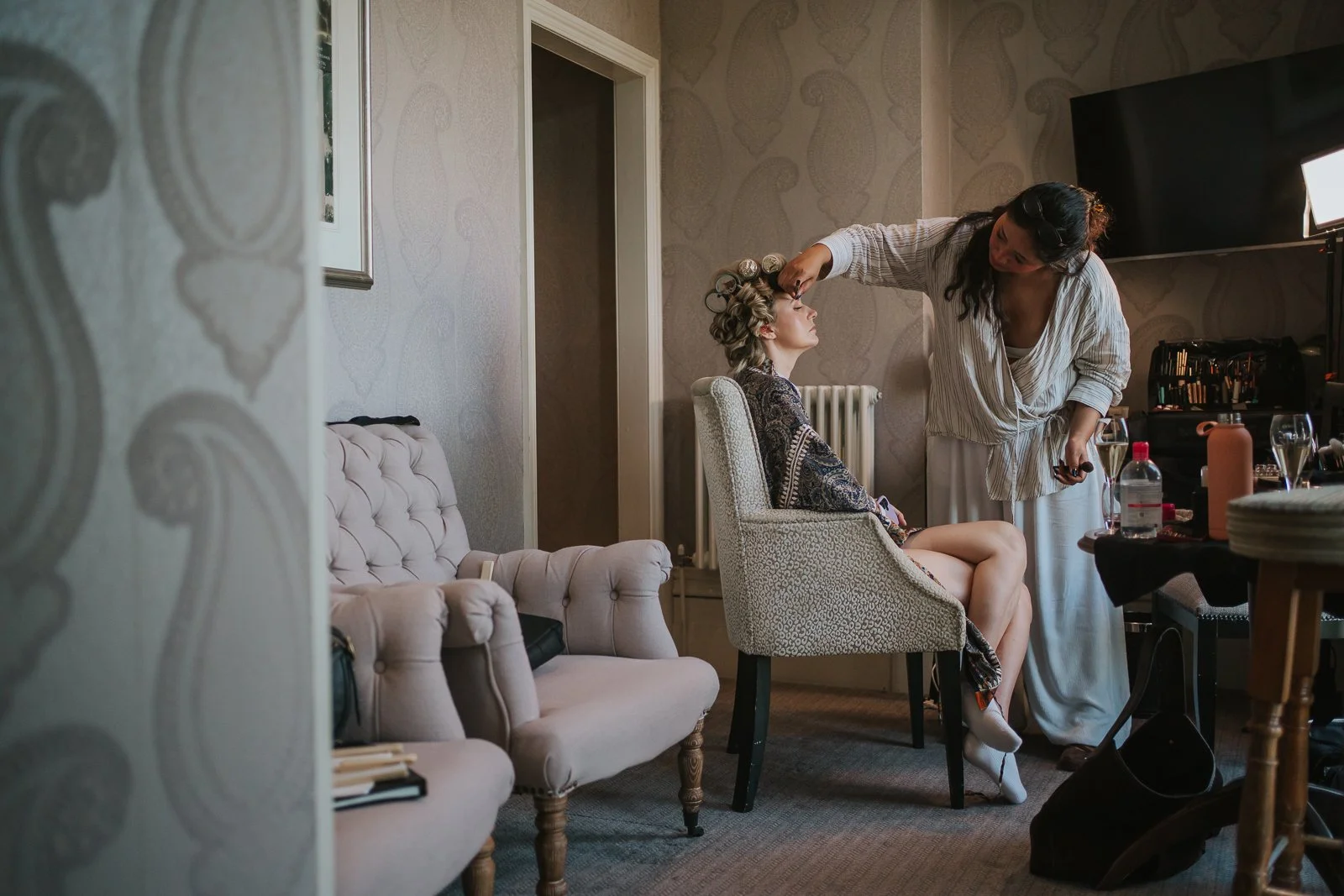  Make-up artist applying the bride's make-up in a beautifully appointed suite at The Petersham Hotel during wedding preparations. 