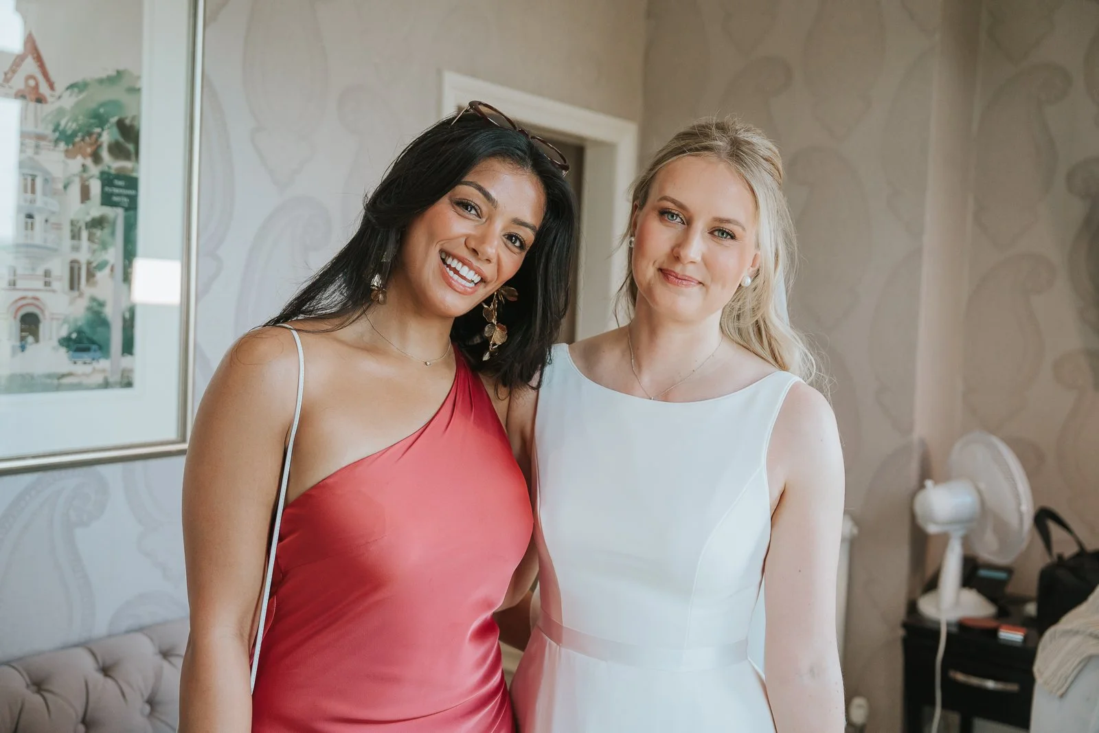  Bride and bridesmaid smiling together in a luxury suite at The Petersham Hotel, Richmond, during relaxed wedding morning preparations. 
