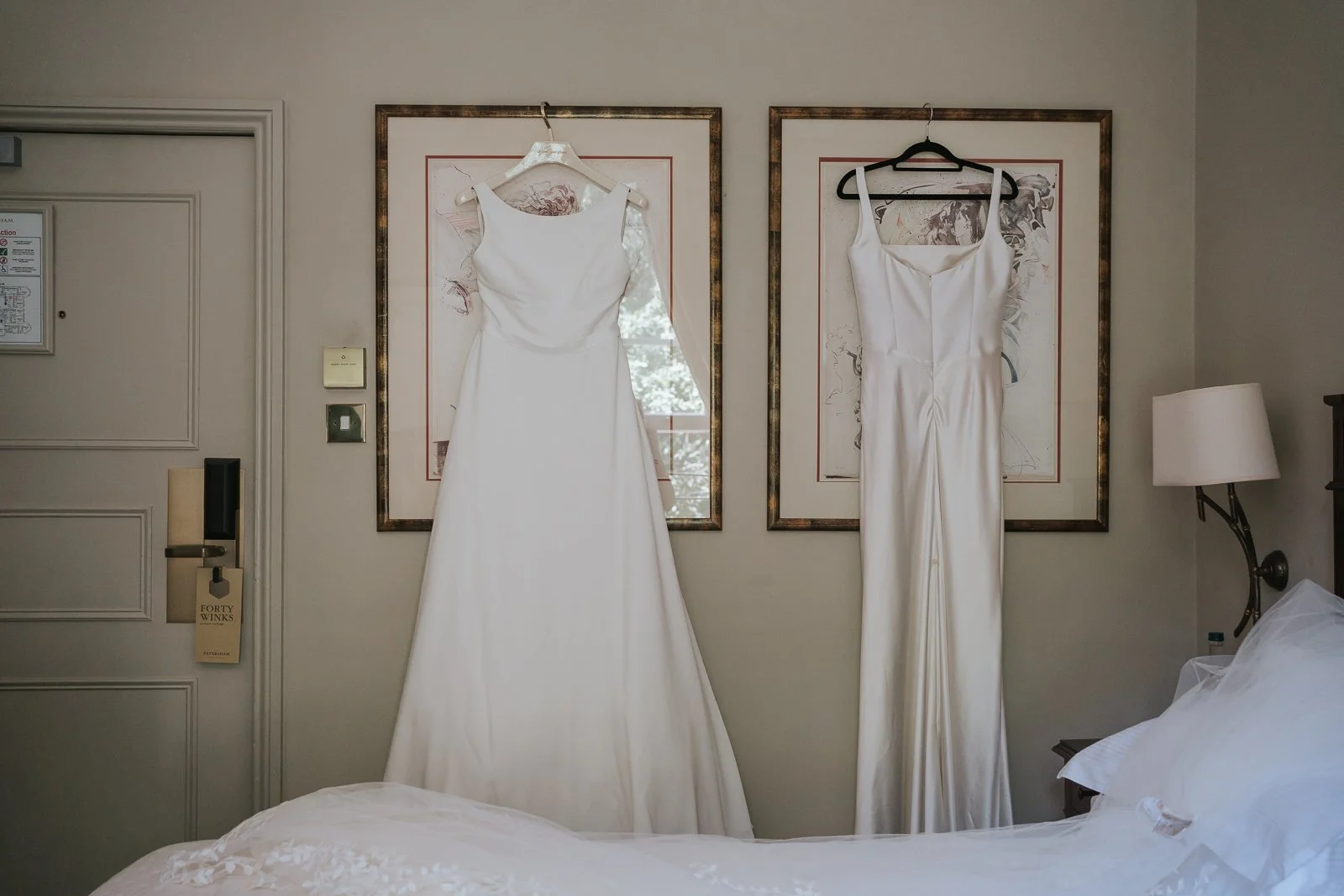  Bride's wedding dress and bridesmaid dress hanging side by side in a luxury room at The Petersham Hotel, ready for a Richmond wedding celebration. 