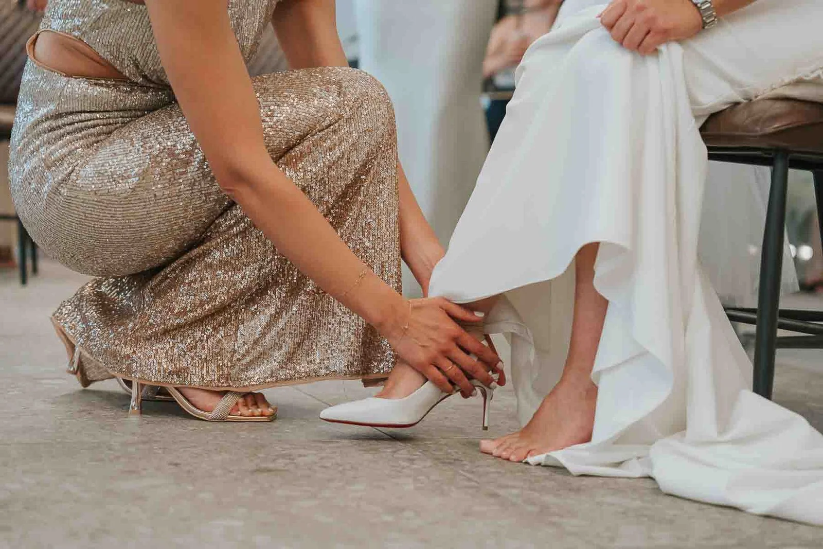  Close-up of a traditional Greek wedding shoe ceremony as a bridesmaid helps the bride into her white wedding heel before the dancing begins. 