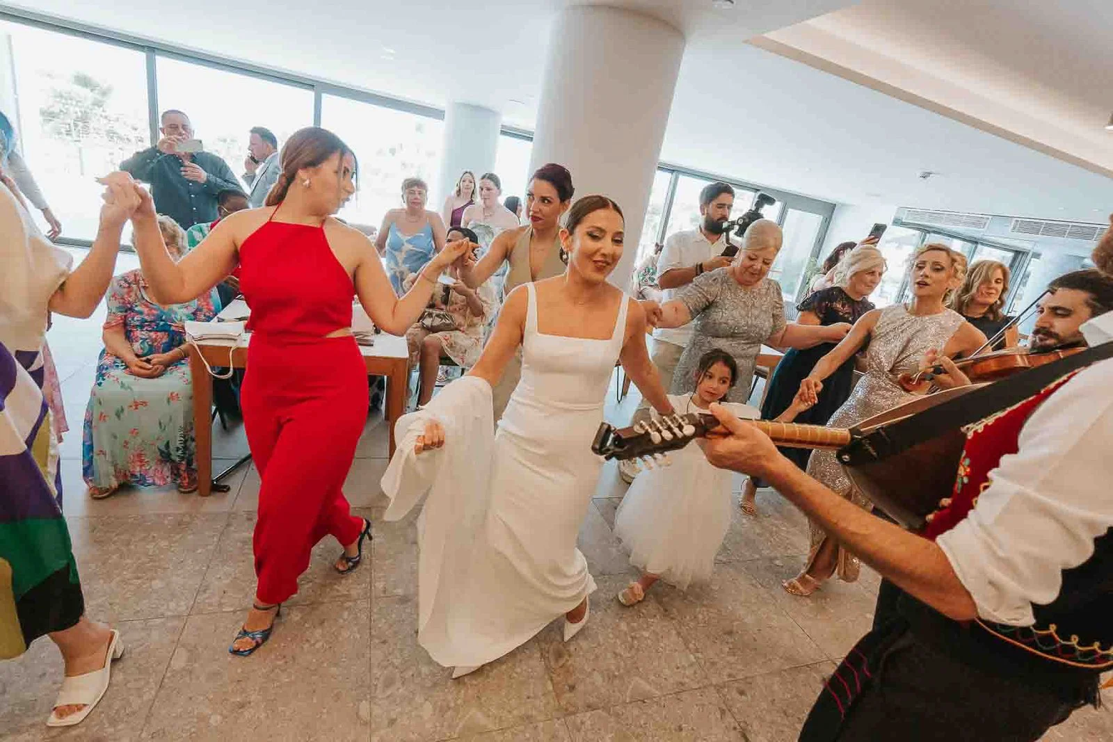  Bride leading a traditional Greek circle dance at her wedding reception, joined by family and friends as live musicians perform. 