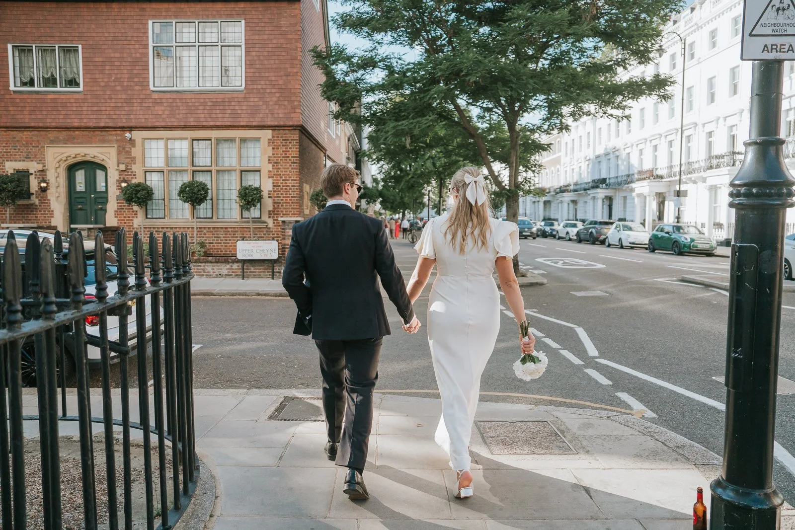  Newly married couple walking together along a quiet Chelsea street, with classic London architecture and leafy avenues creating a timeless backdrop for natural wedding photography. 