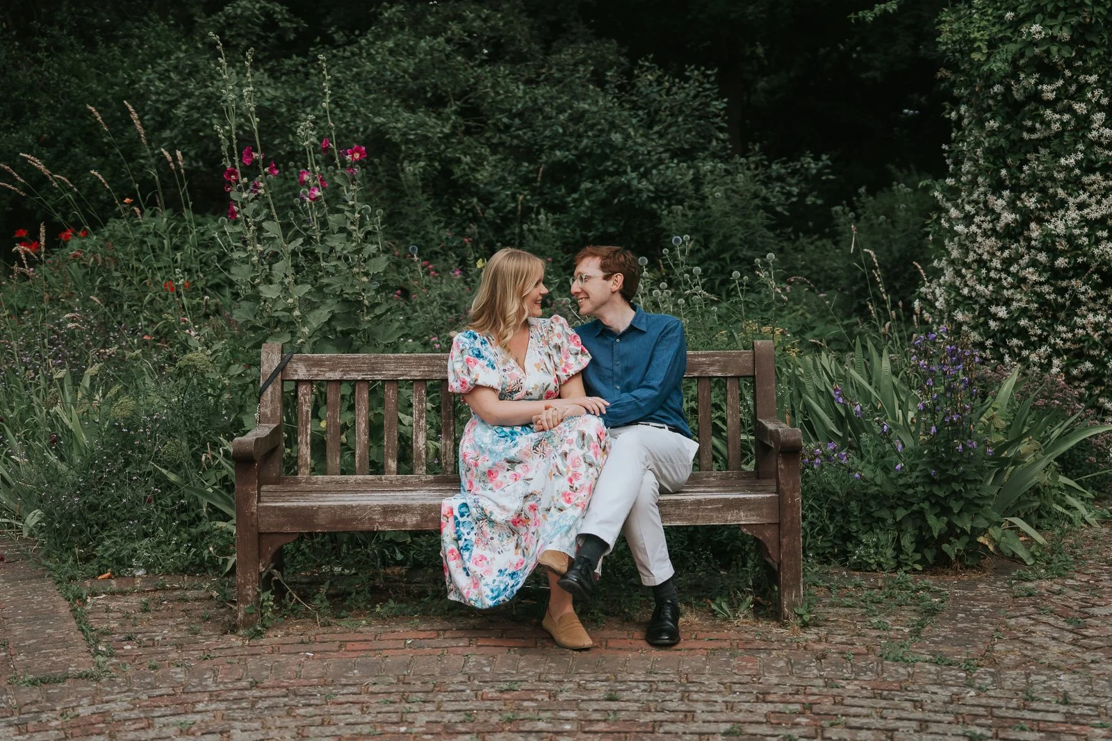  Couple sitting on a garden bench during their engagement photoshoot in Battersea Park, London, enjoying a relaxed and intimate moment among colourful flower borders. 