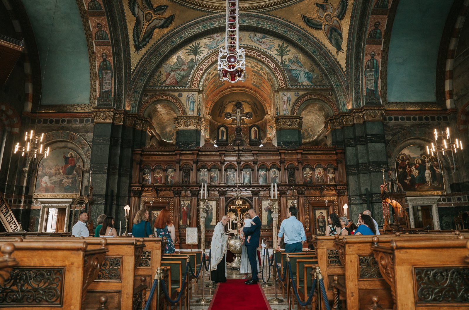  Greek Christening in front of the ornate iconostasis and altar inside Saint Sofia Greek Orthodox Cathedral in Bayswater London with religious icons, carved wood and marble columns 