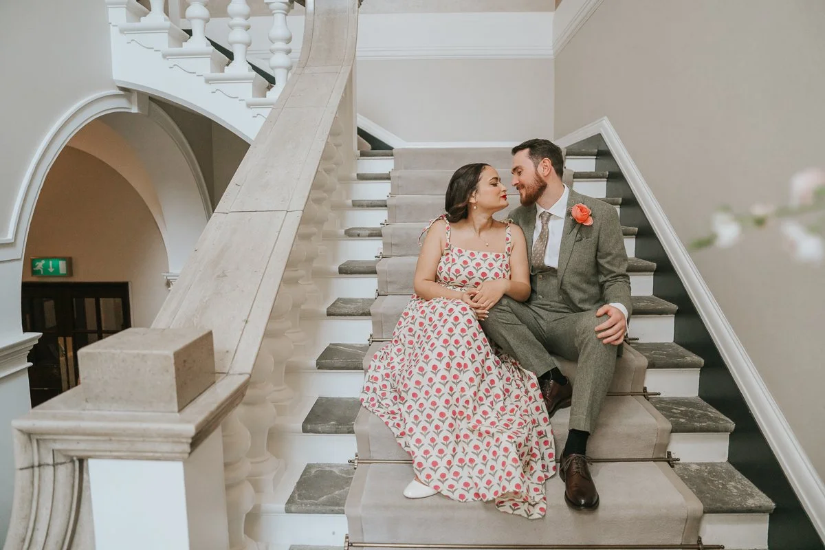  Bride and groom sharing a quiet moment on the grand staircase in the waiting area at Chelsea Old Town Hall, with elegant architecture providing a timeless backdrop for intimate wedding photography. 