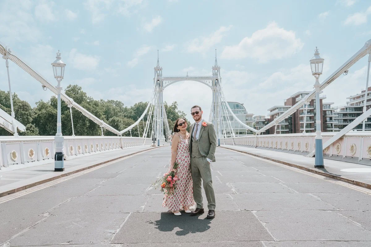  Newly married couple posing on the iconic Albert Bridge in Chelsea, London, with the elegant white suspension bridge creating a timeless backdrop for natural wedding photography. 