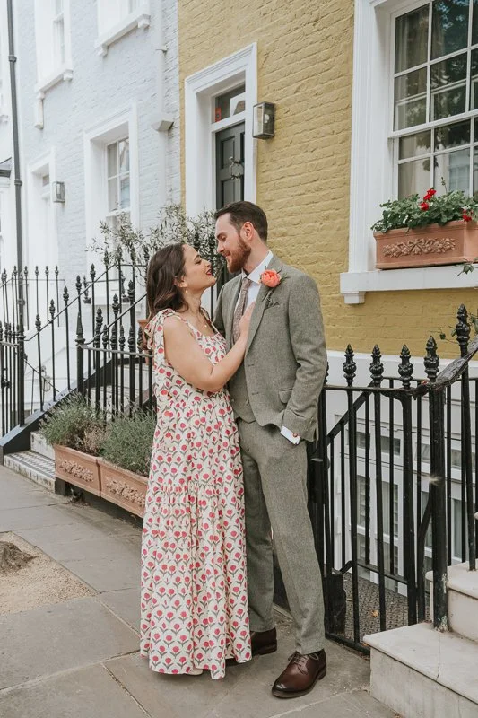  Newly married couple sharing a romantic moment outside a charming Chelsea townhouse, surrounded by colourful façades and classic London architecture during their post-ceremony photoshoot. 