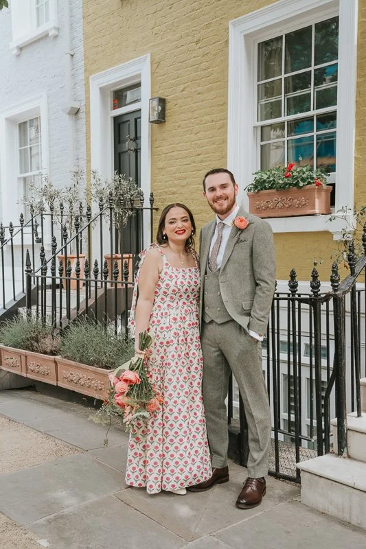  Bride and groom posing outside a pastel-coloured Chelsea townhouse, with elegant Georgian architecture creating a timeless backdrop for relaxed Chelsea wedding photography. 