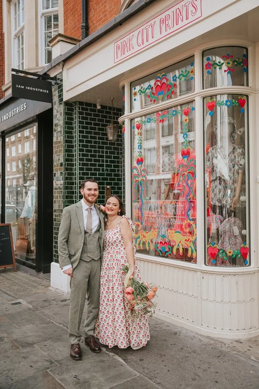  Bride and groom posing outside the colourful Pink City Prints boutique on King's Road, Chelsea, adding a fun and stylish London backdrop to their relaxed wedding photography session. 
