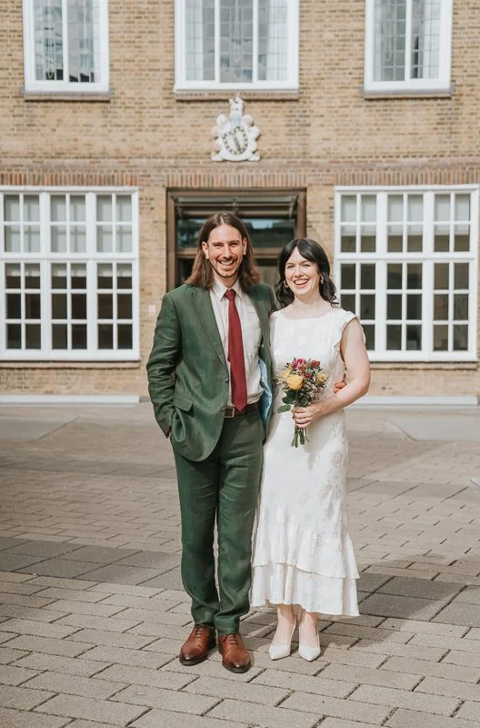  Bride and groom outside  Lambeth Town Hall in Brixton , smiling together after their London wedding ceremony with the historic town hall façade in the background. 