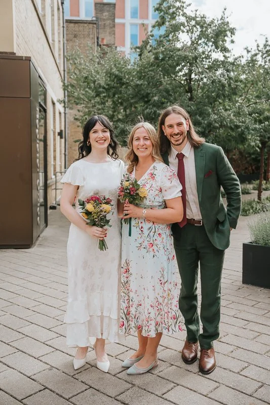  Bride and groom posing with a family member outside  Lambeth Town Hall in Brixton  following their London registry office wedding, surrounded by the modern courtyard gardens. 