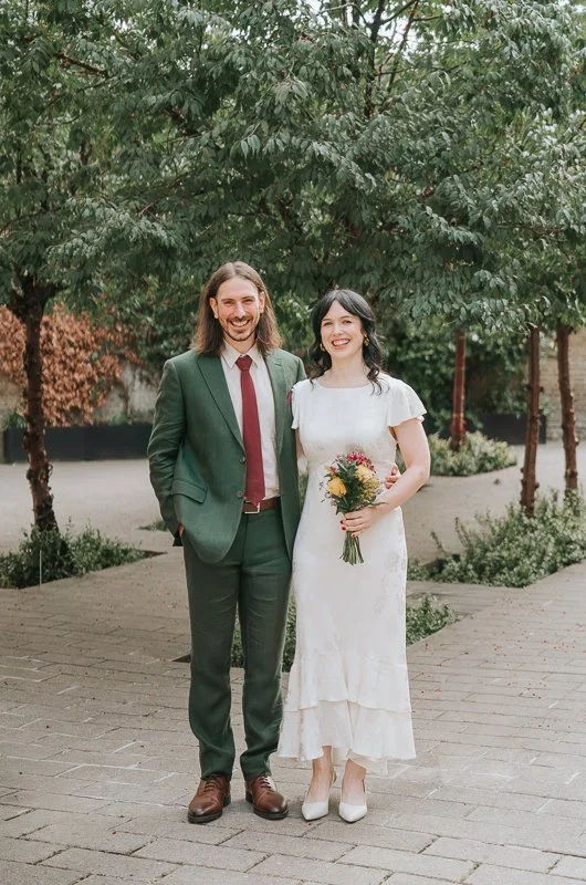  Newly married couple posing together in the landscaped courtyard outside  Lambeth Town Hall, Brixton , holding a colourful bouquet after their intimate London wedding ceremony. 