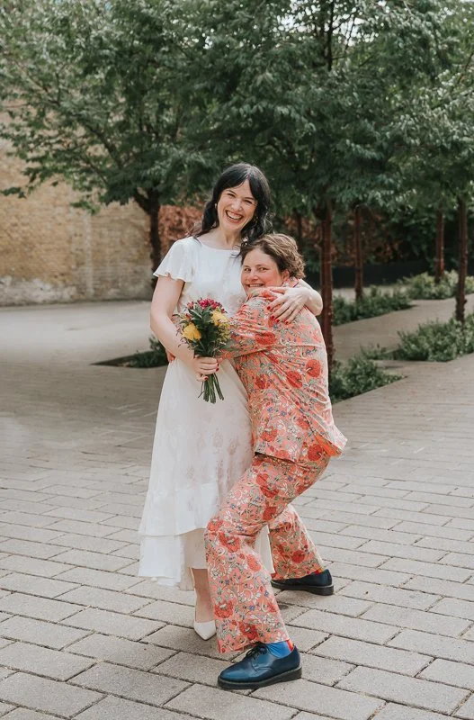  Relaxed documentary wedding photograph of the bride sharing a joyful hug with a guest outside  Lambeth Town Hall in Brixton , capturing a fun candid moment after the ceremony. 