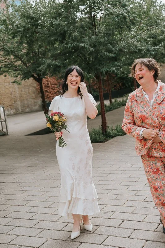  Relaxed documentary wedding photograph of the bride sharing a joyful hug with a guest outside  Lambeth Town Hall in Brixton , capturing a fun candid moment after the ceremony. 