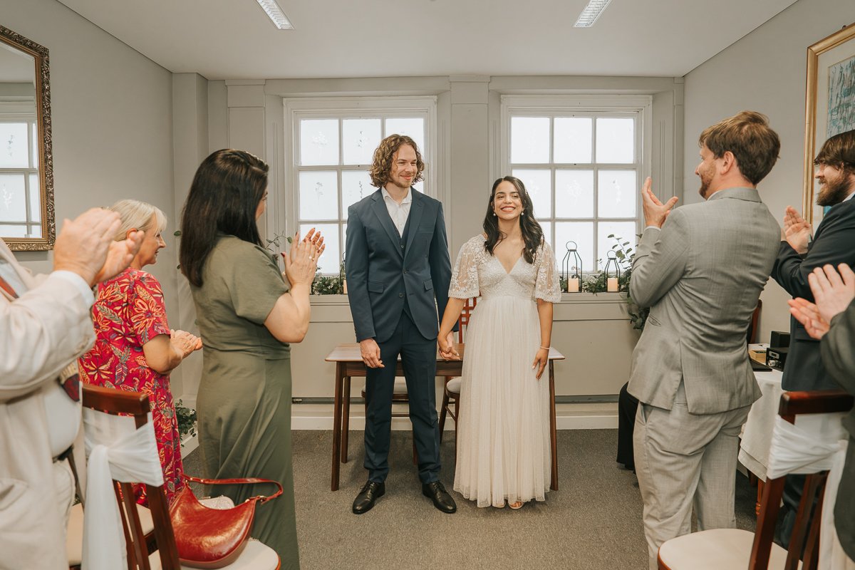  Newly married couple holding hands as guests applaud after their Kingston Register Office wedding ceremony. 