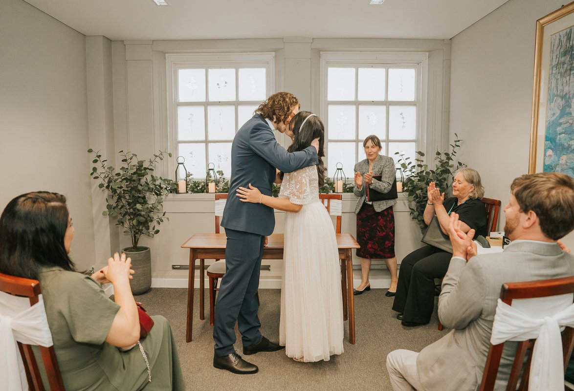  Bride and groom sharing their first kiss during a joyful wedding ceremony at Kingston Register Office. 