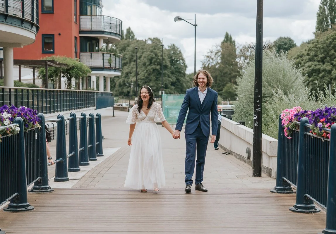  Newly married couple strolling along Kingston riverside surrounded by colourful flowers, capturing natural wedding photography in Kingston upon Thames. 