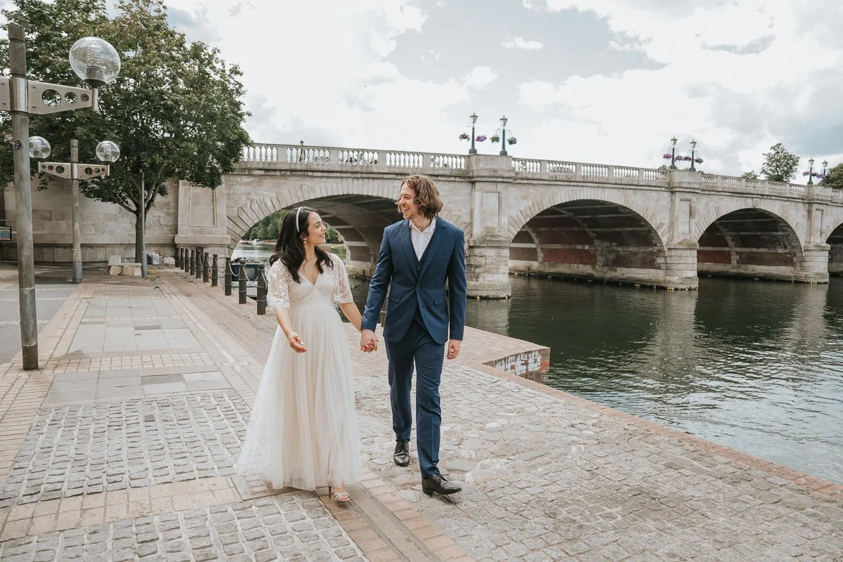  Romantic wedding photos of the bride and groom walking beside the River Thames with Kingston Bridge creating a stunning backdrop. 