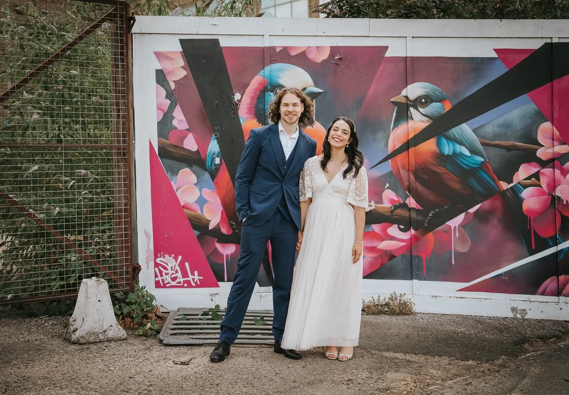  Newly married couple posing in front of colourful street art along Kingston riverside, showcasing creative wedding photography ideas in Kingston. 
