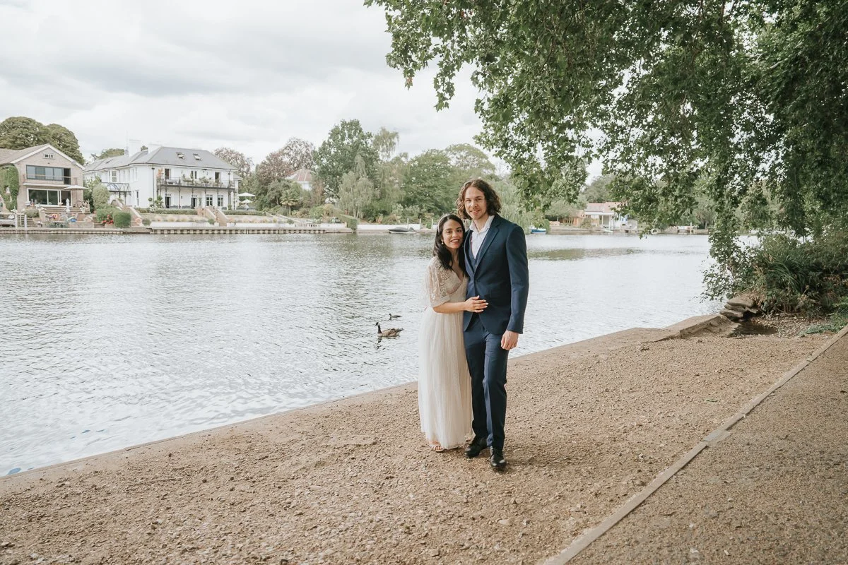  Bride and groom standing beneath leafy riverside trees overlooking the Thames after their Kingston Register Office wedding ceremony. 
