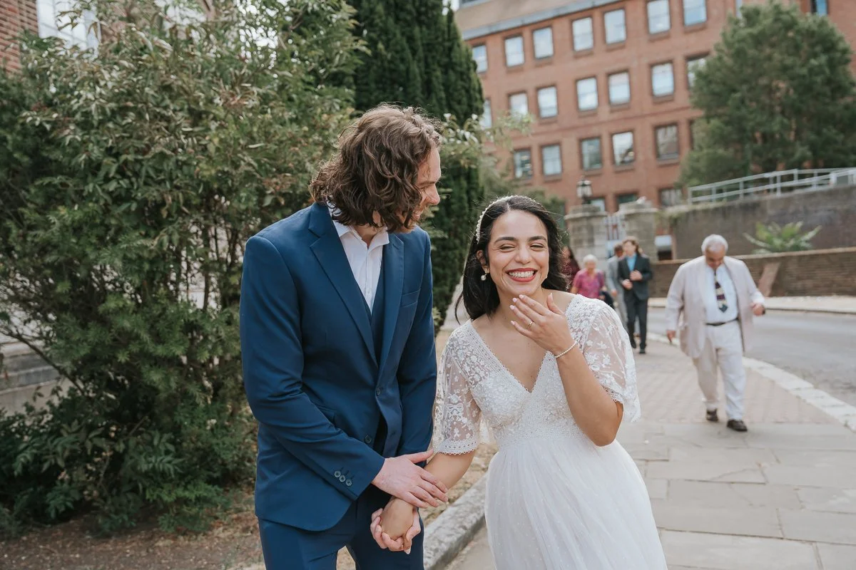  Bride and groom laughing together outside Kingston Register Office moments after their intimate civil wedding ceremony in Kingston upon Thames. 