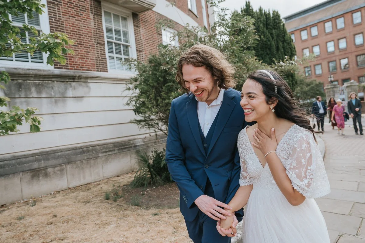  Natural wedding photography of the newly married couple walking hand in hand outside Kingston Register Office, sharing a joyful moment. 