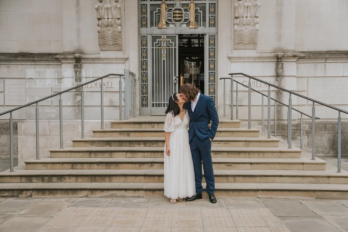  Romantic portrait of the bride and groom sharing a kiss on the steps outside Kingston Register Office after exchanging their vows. 