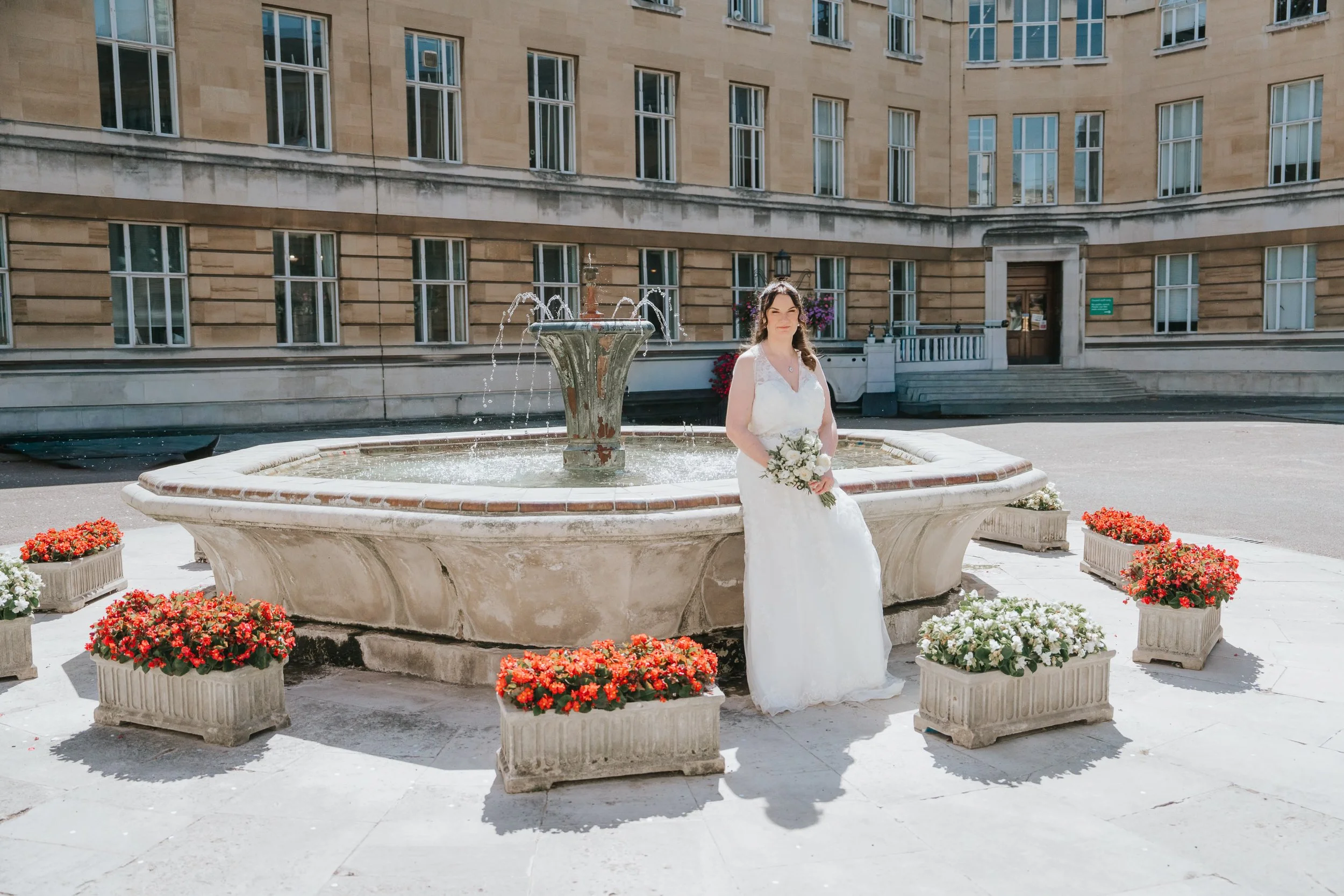  Bride holding her wedding bouquet beside the fountain in the courtyard at Wandsworth Town Hall, London. 
