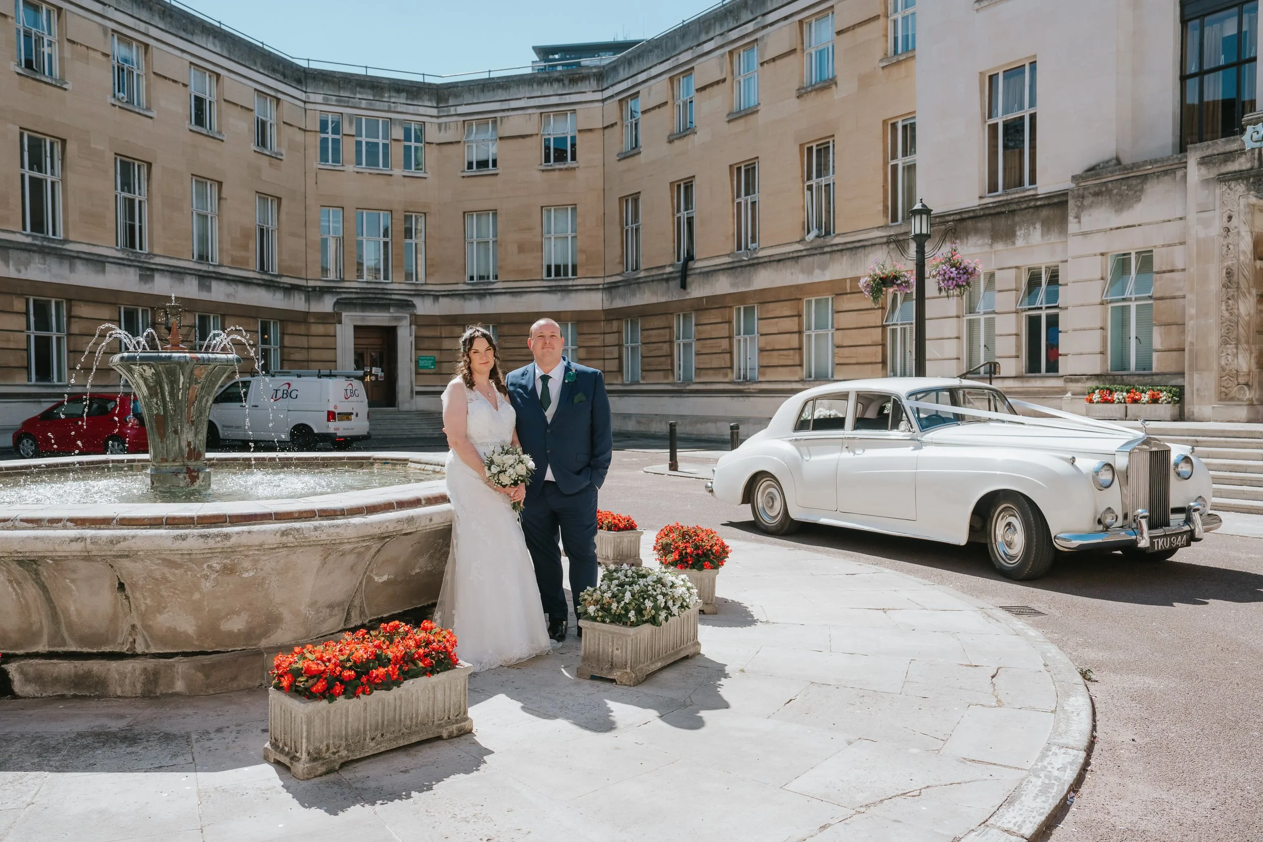  Bride and groom beside the fountain and a classic white wedding car in the courtyard at Wandsworth Town Hall. 