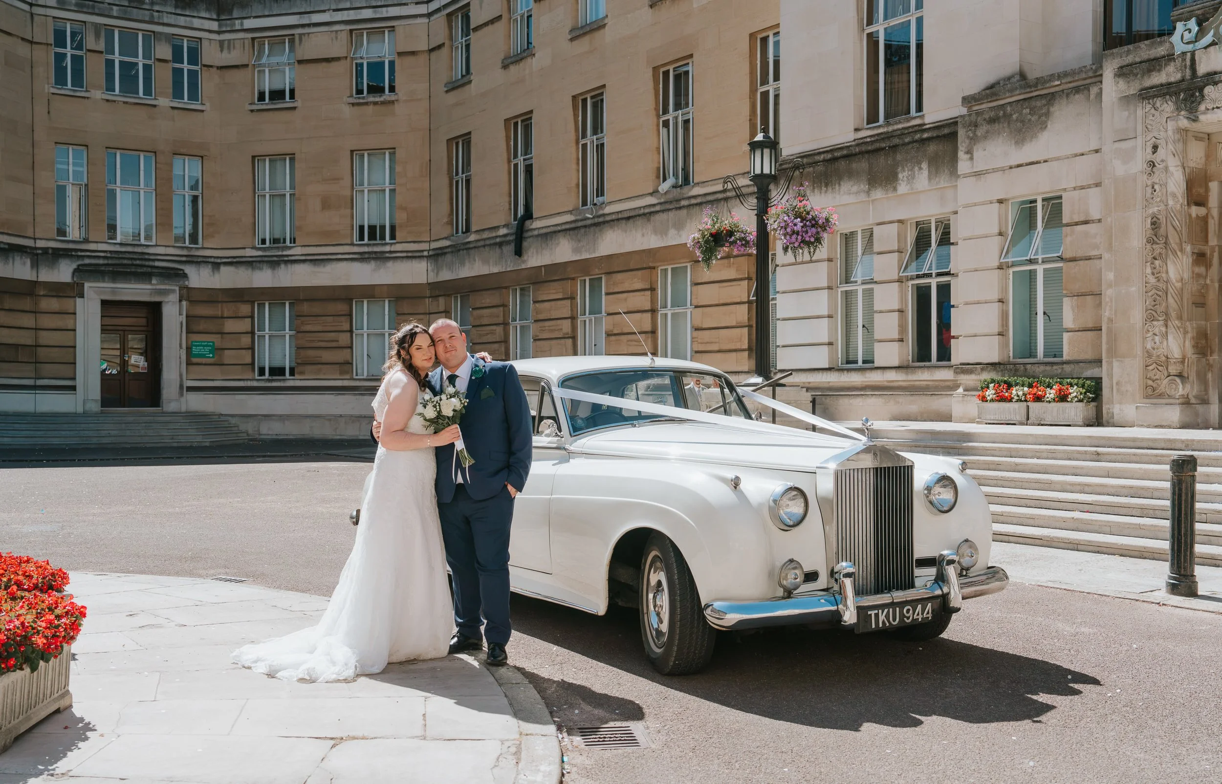  Newly married couple posing beside a classic white Rolls-Royce wedding car outside Wandsworth Town Hall. 