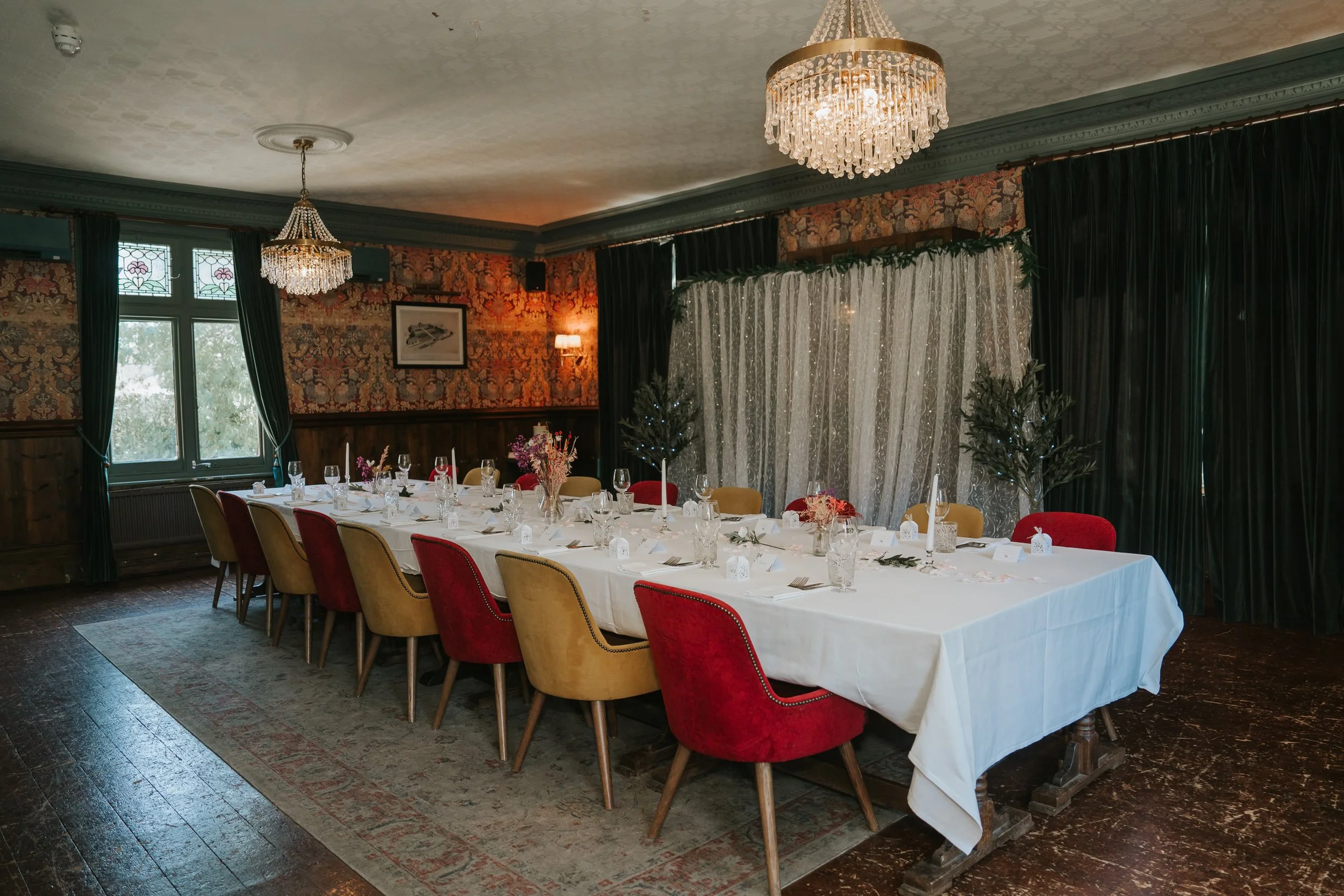  The Trinity Room at the County Arms pub in Wandsworth, arranged for an intimate wedding reception with long tables, colourful chairs and chandeliers. 