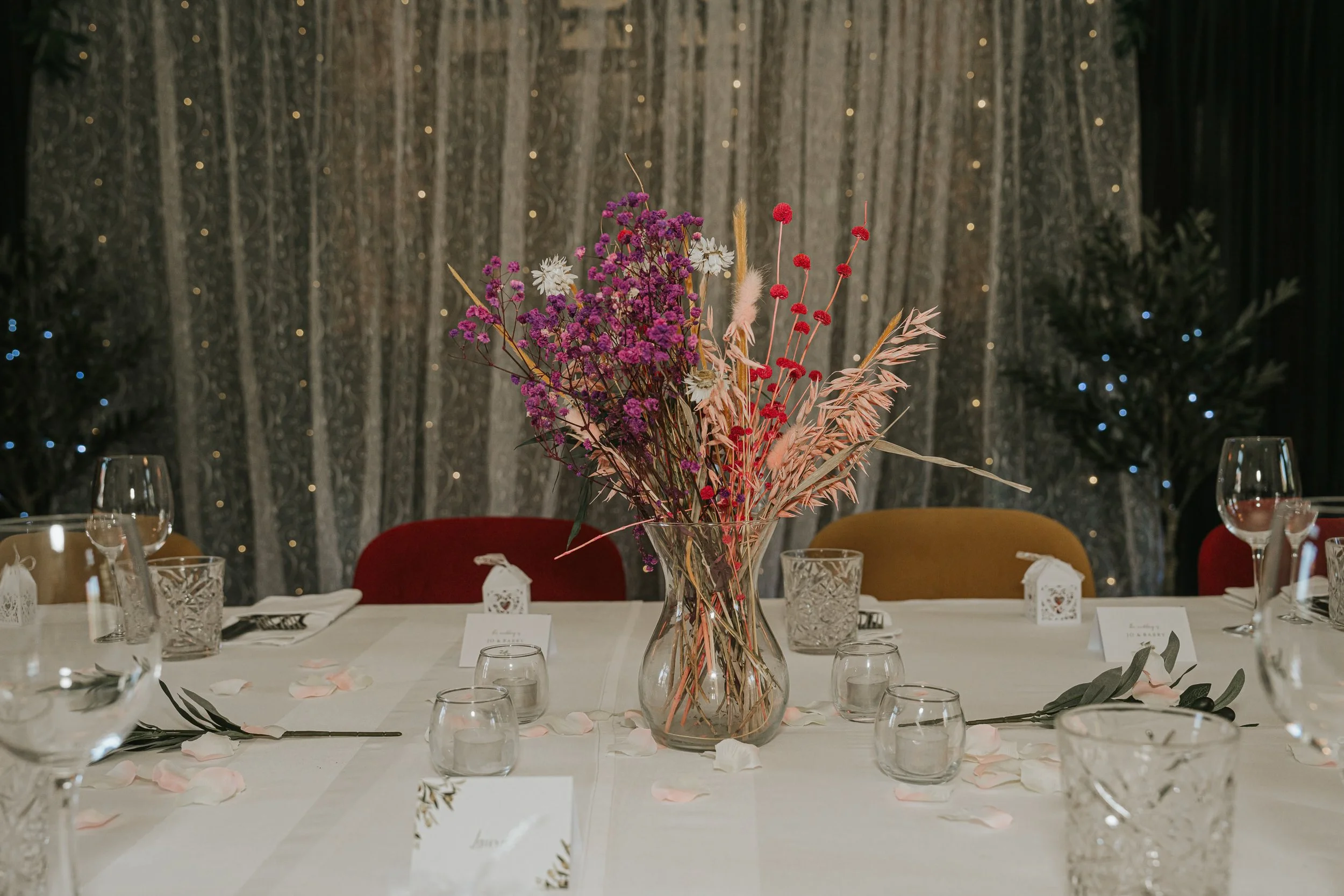 Dried-flower wedding centrepiece displayed against a lace and fairy-light backdrop in the Trinity Room at the County Arms. 