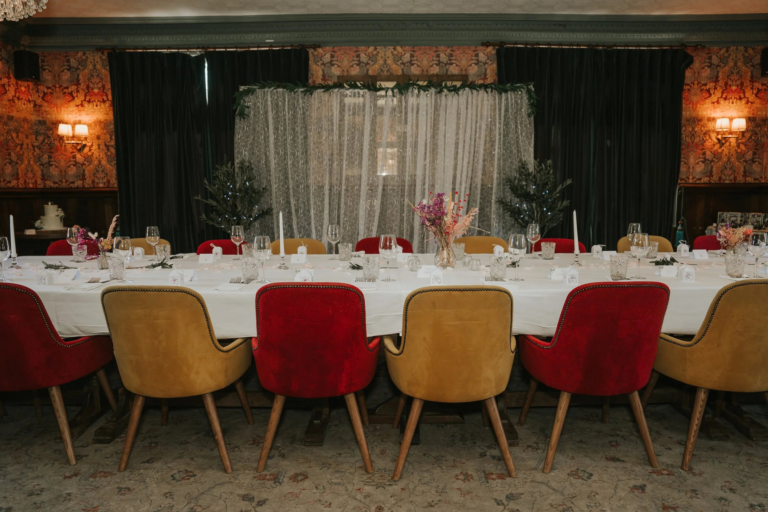  Long wedding reception table with red and gold chairs, flowers and candles in the Trinity Room at the County Arms pub. 