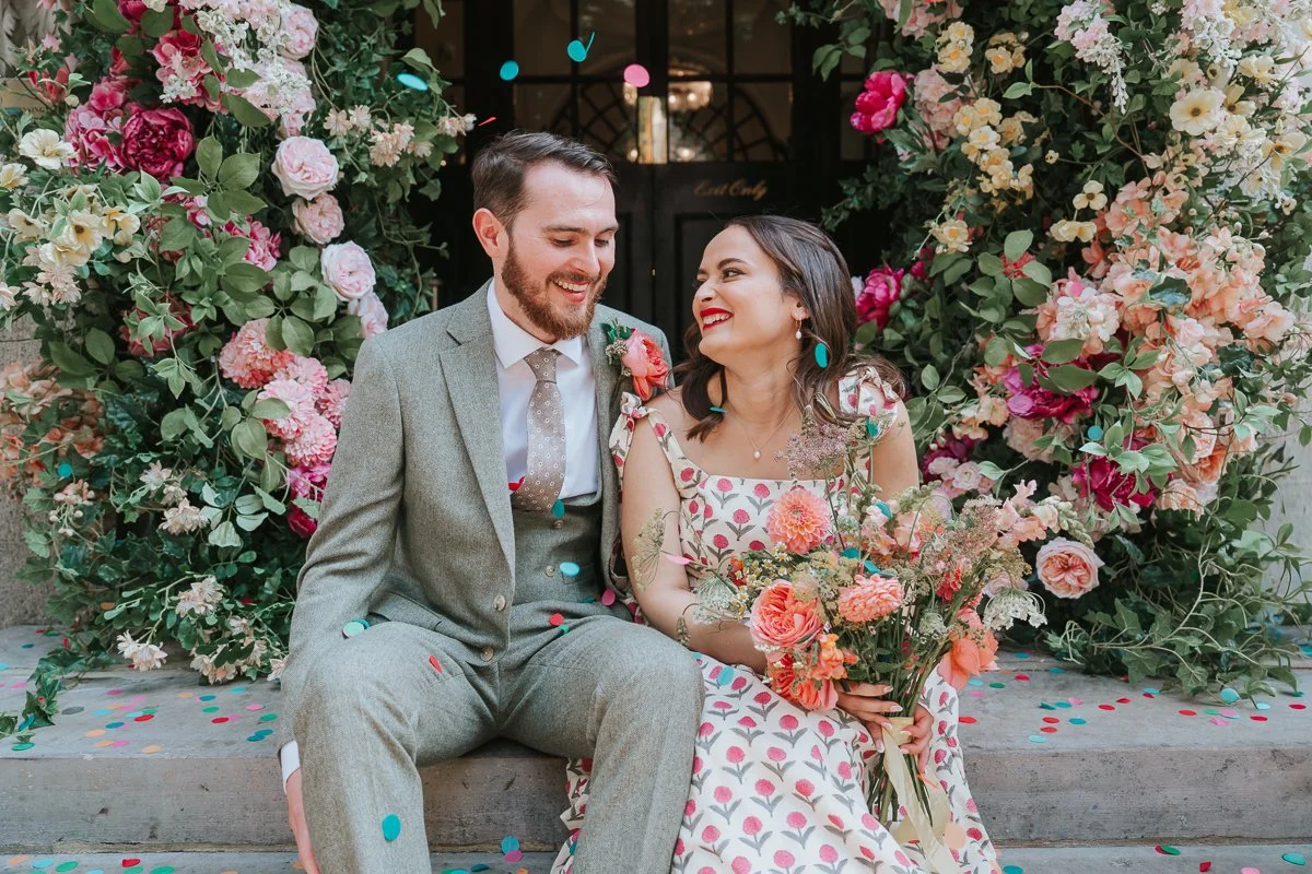  Bride and groom pose for photograph sitting on steps outside Chelsea Old Town Hall after their wedding. 