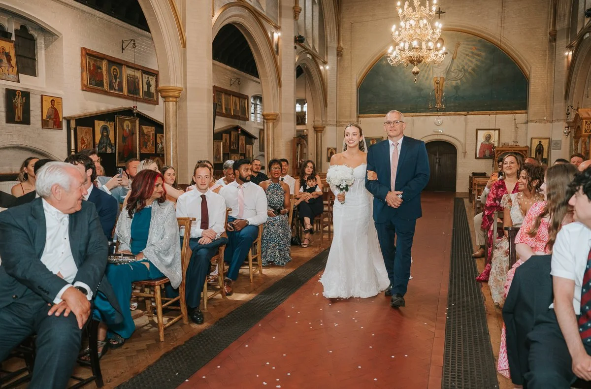  Bride walking down the aisle with her father at the Greek Orthodox Church of Saint Nectarios in Battersea. 