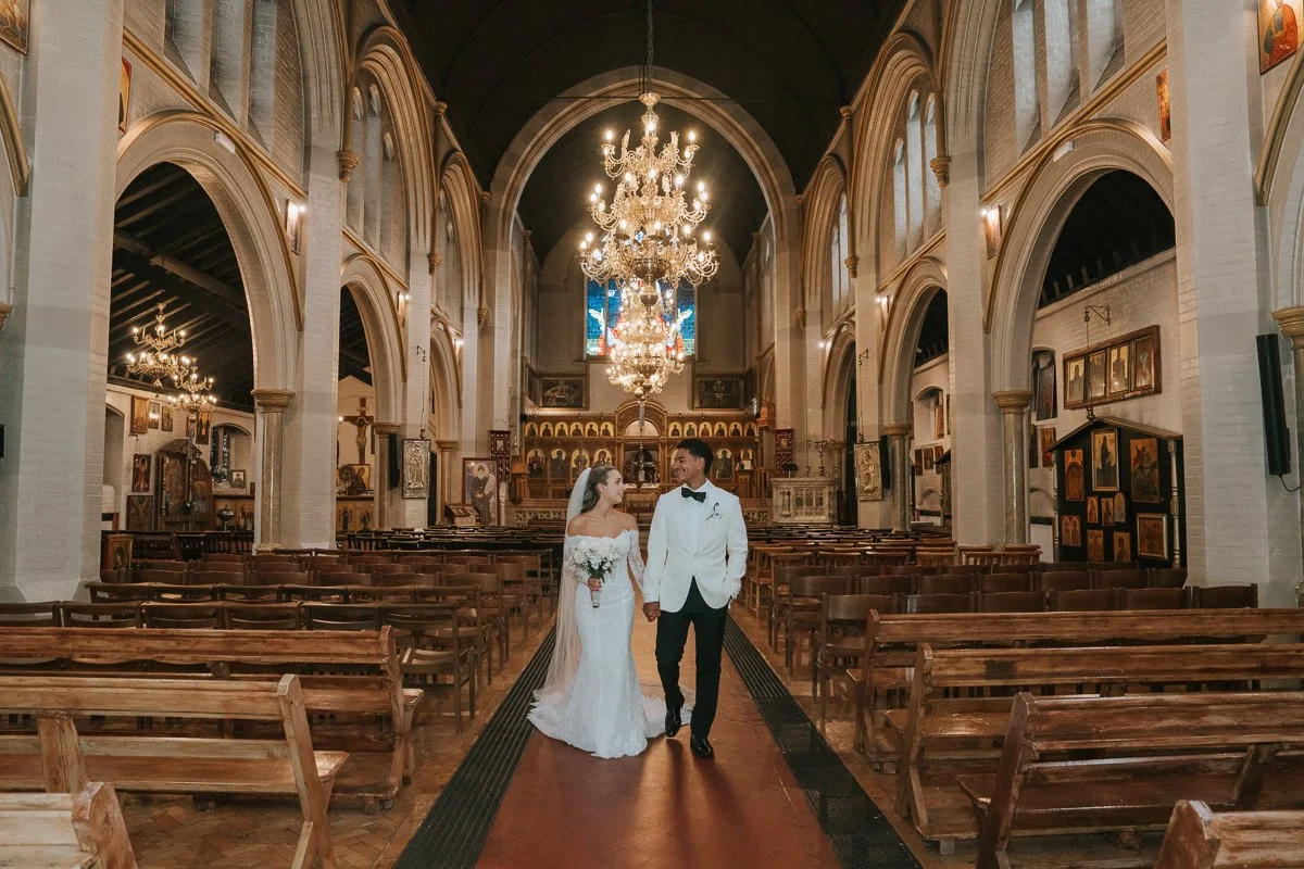 Bride and groom walking together through the beautiful interior of Saint Nectarios Greek Orthodox Church in Battersea after their wedding ceremony. 