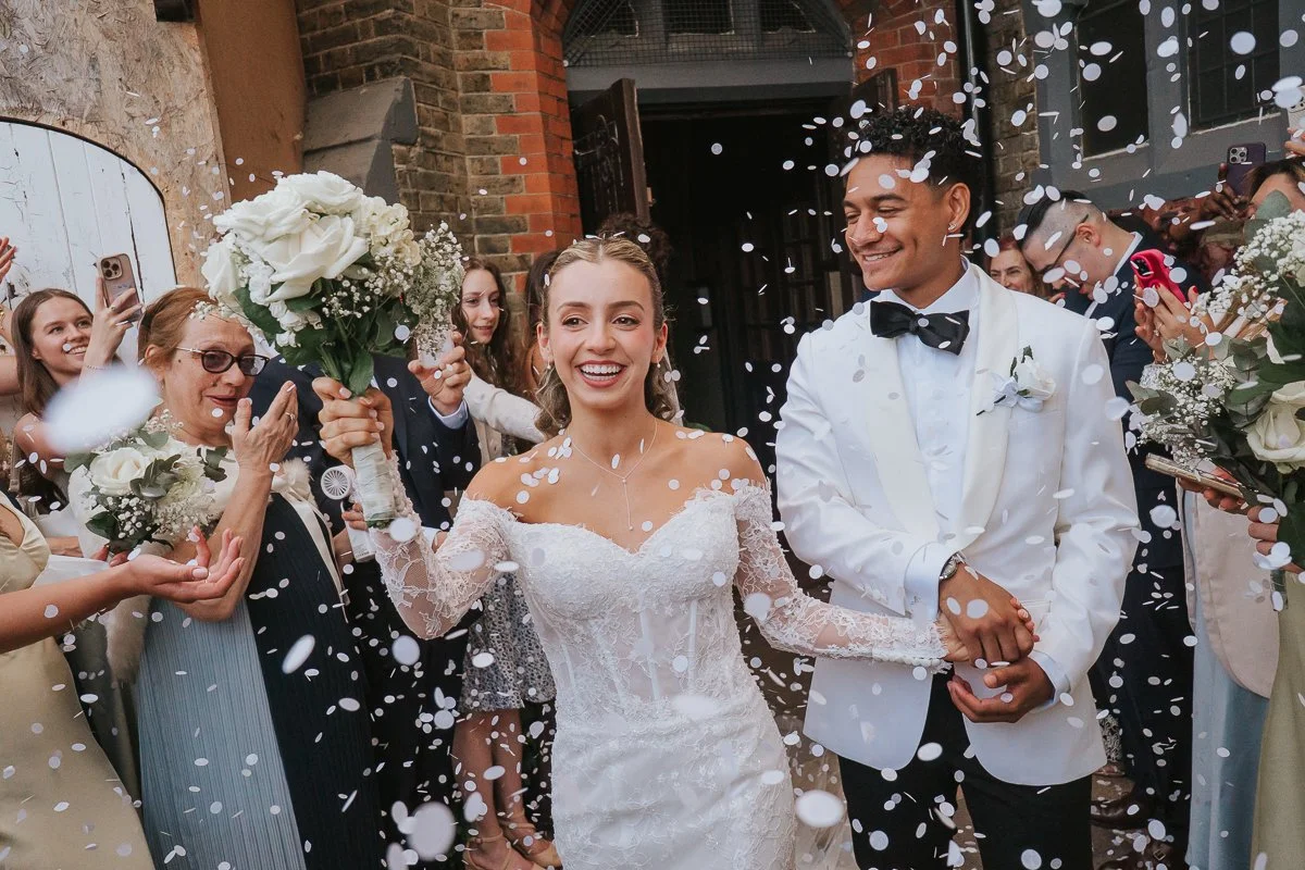  Joyful bride and groom surrounded by confetti outside Saint Nectarios Greek Orthodox Church following their London wedding. 